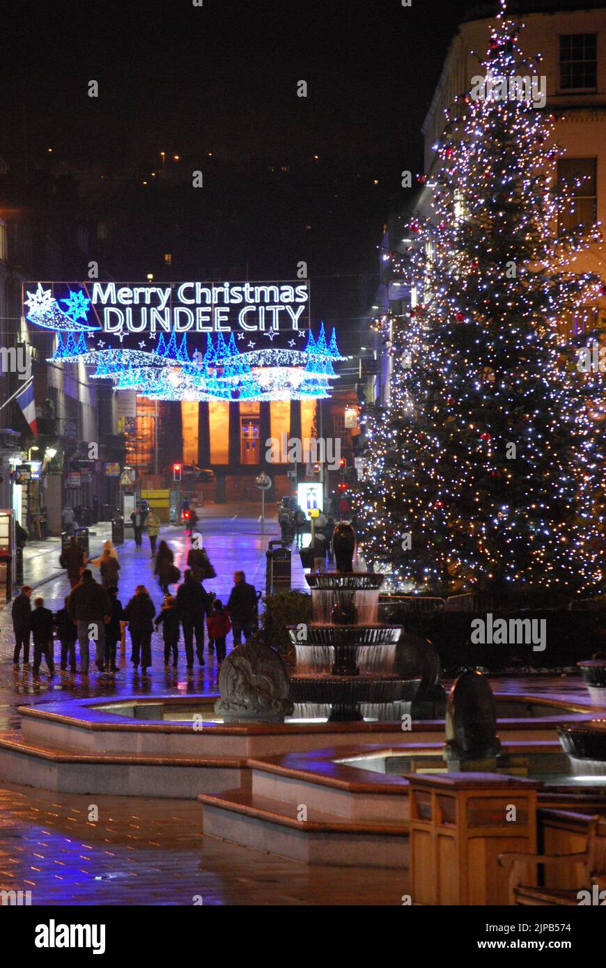 „Merry Christmas Dundee City“, nächtliche Straßenszene mit Weihnachtsbaum, Brunnen und Lichtern, während die Menschen die Reform Street entlang zur High School of Dundee gehen Stockfoto