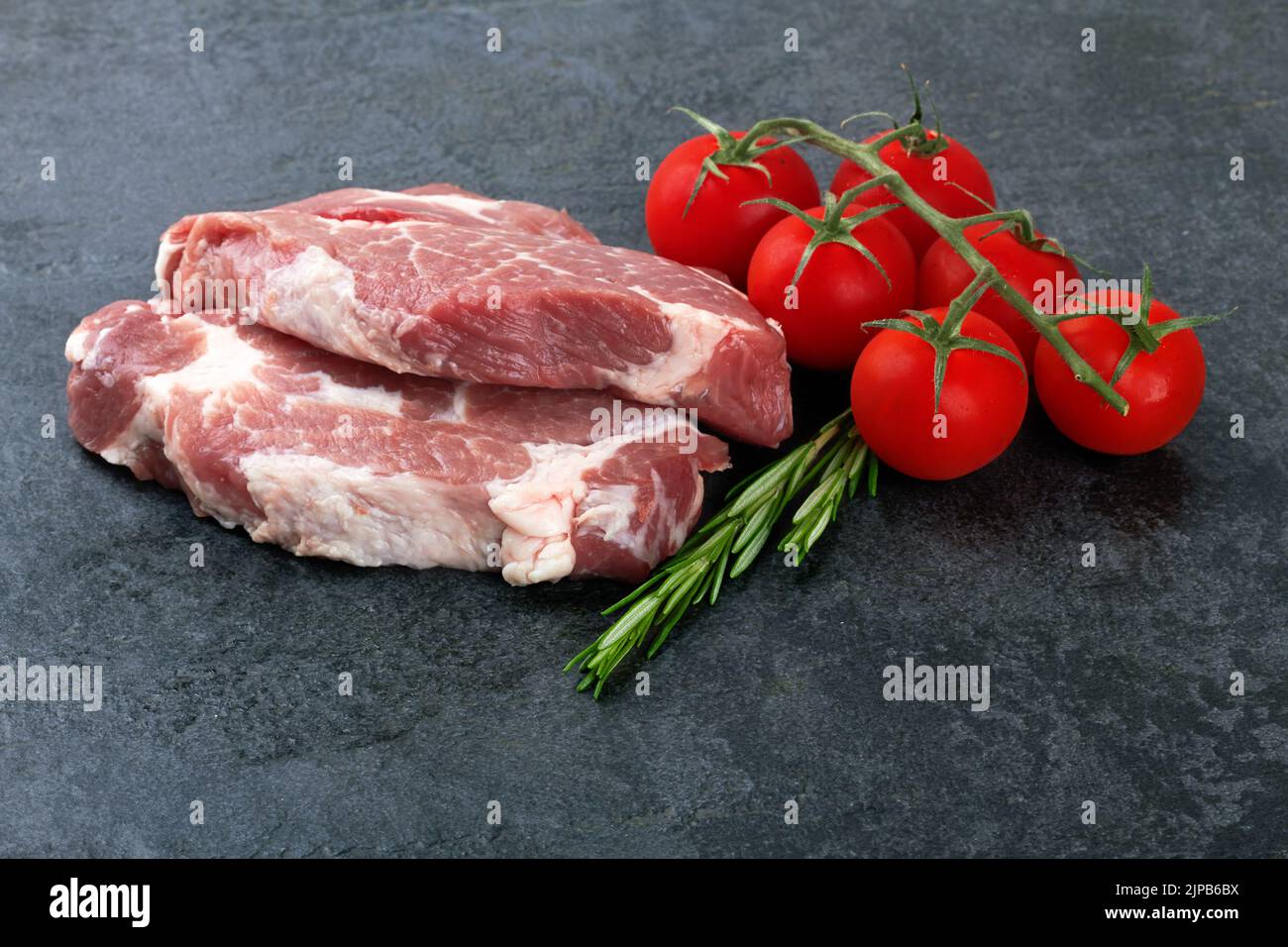 Rohes Fleisch mit Tomaten auf schwarzer Oberfläche Stockfoto