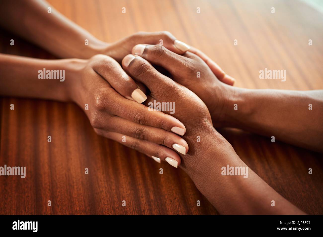 Das muss man nicht alleine durchmachen. Nahaufnahme von zwei Händen, die sich nicht wiedererkennen lassen, während sie sich auf einem Holztisch ausruhen. Stockfoto