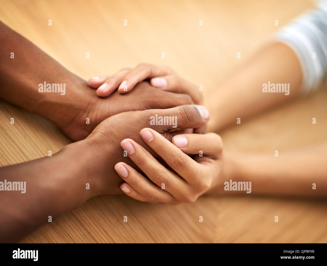 Manchmal braucht man nur eine helfende Hand. Zwei unkenntliche Menschen halten sich die Hände, während sie tagsüber an einem Tisch sitzen. Stockfoto