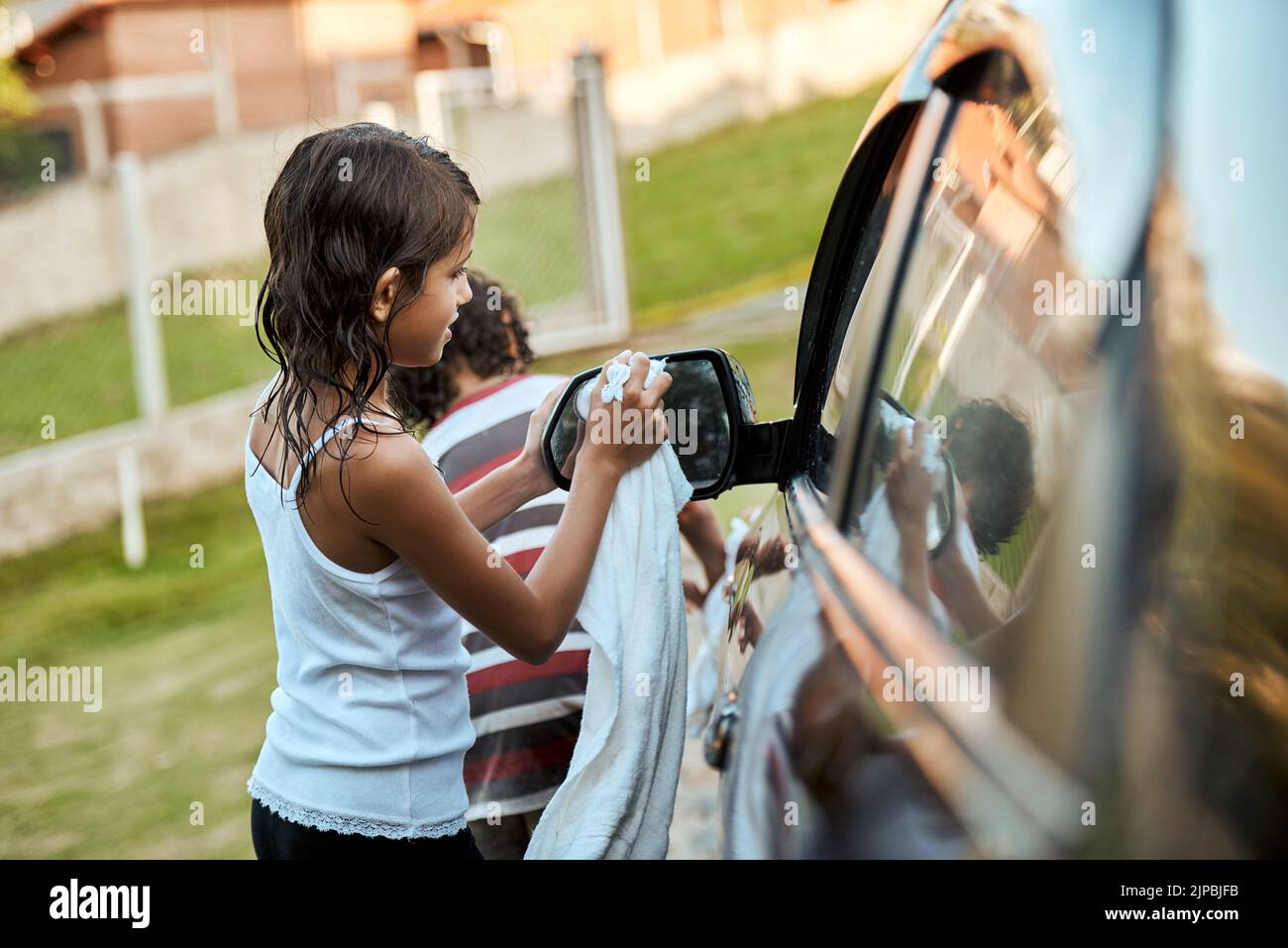 Zwei fröhliche Kinder waschen tagsüber ihr Elternauto gemeinsam draußen. Stockfoto