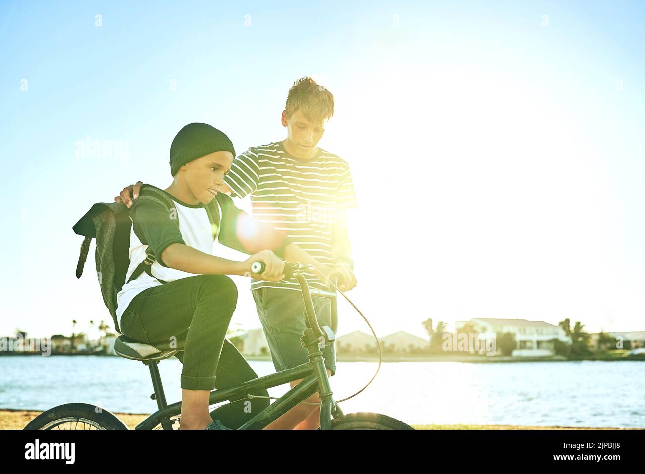 Es ist das, was ältere Brüder tun. Ein kleiner Junge lehrt seinen jüngeren Bruder, wie man Fahrrad entlang einer Lagune fahren. Stockfoto