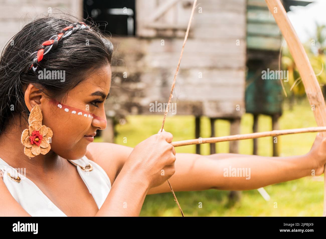 Ein indigenes Teenager-Mädchen mit einem gemalten Gesicht und schießem Pfeil mit einem Holzbogen in einer norkaribischen Gemeinde in Nicaragua. Stockfoto