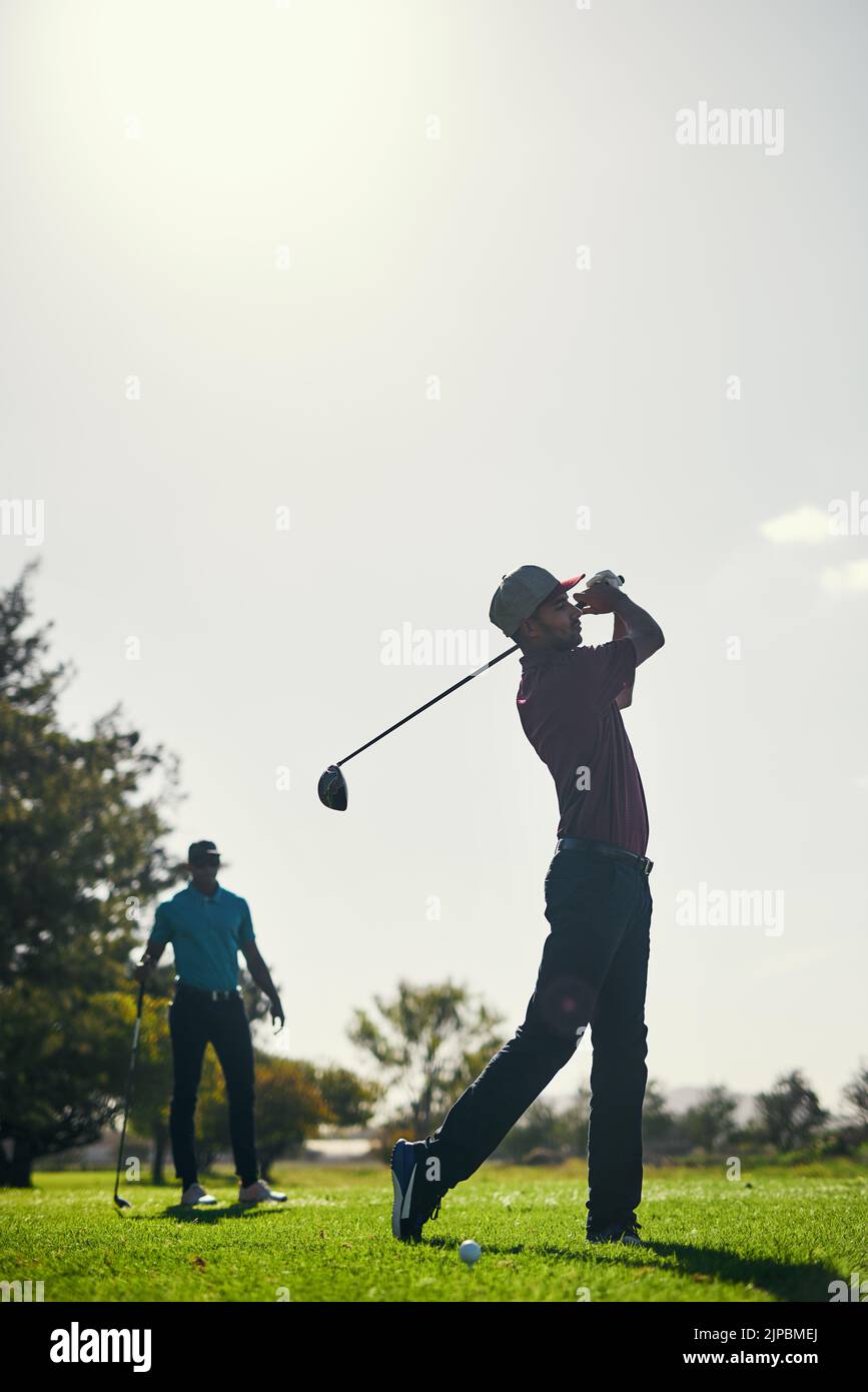 Ihre Technik ist beeindruckend. Ein fokussierter junger Golfer im Begriff, mit seinem Golfschläger draußen auf einem Golfplatz zu schwingen und einen Schuss zu spielen. Stockfoto