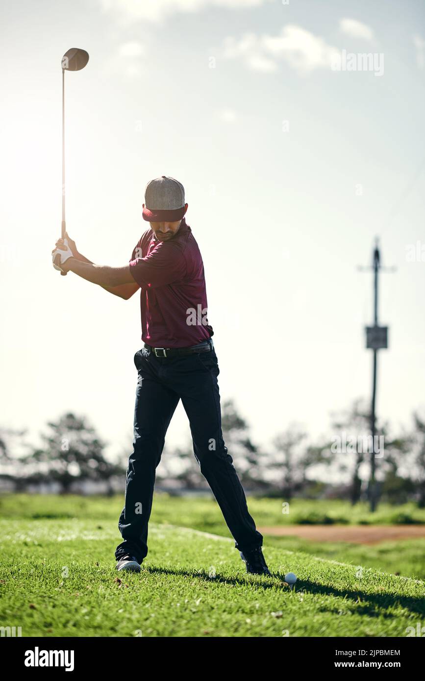 Ziehen Sie sich zurück und schwingen Sie. Ein fokussierter junger Golfer, der kurz davor steht, draußen auf einem Golfplatz mit seinem Golfschläger zu schwingen und einen Schuss zu spielen. Stockfoto