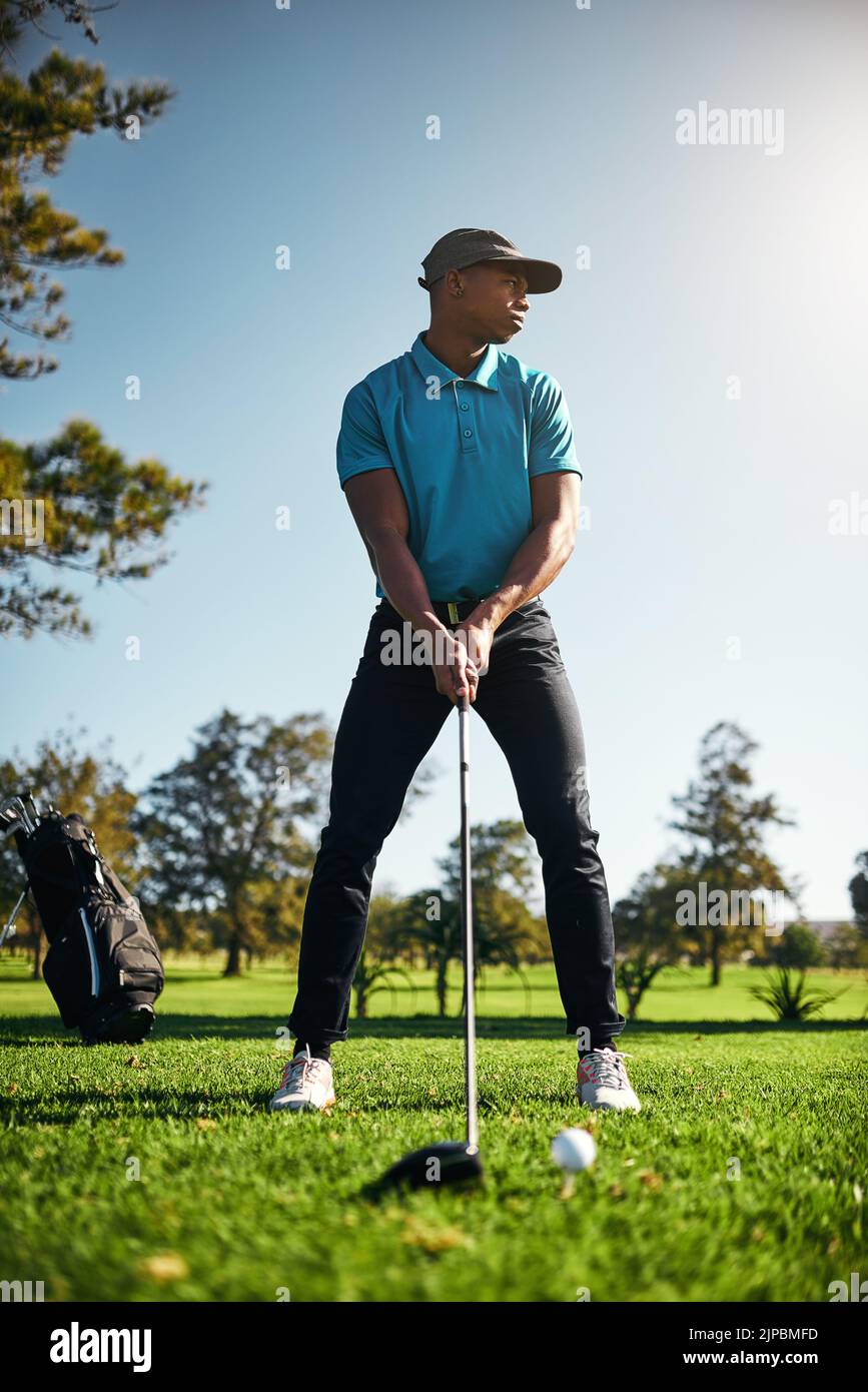 Ein fokussierter junger Golfer, der kurz davor steht, mit seinem Golfschläger draußen auf einem Golfplatz zu schwingen und einen Schuss zu spielen. Stockfoto
