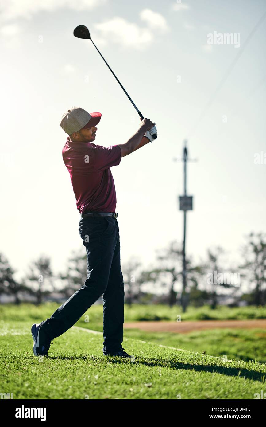 Dieser geht in die Berge. Ein fokussierter junger Golfer im Begriff zu schwingen und einen Schuss mit seinem Golfclub draußen auf einem Kurs zu spielen. Stockfoto