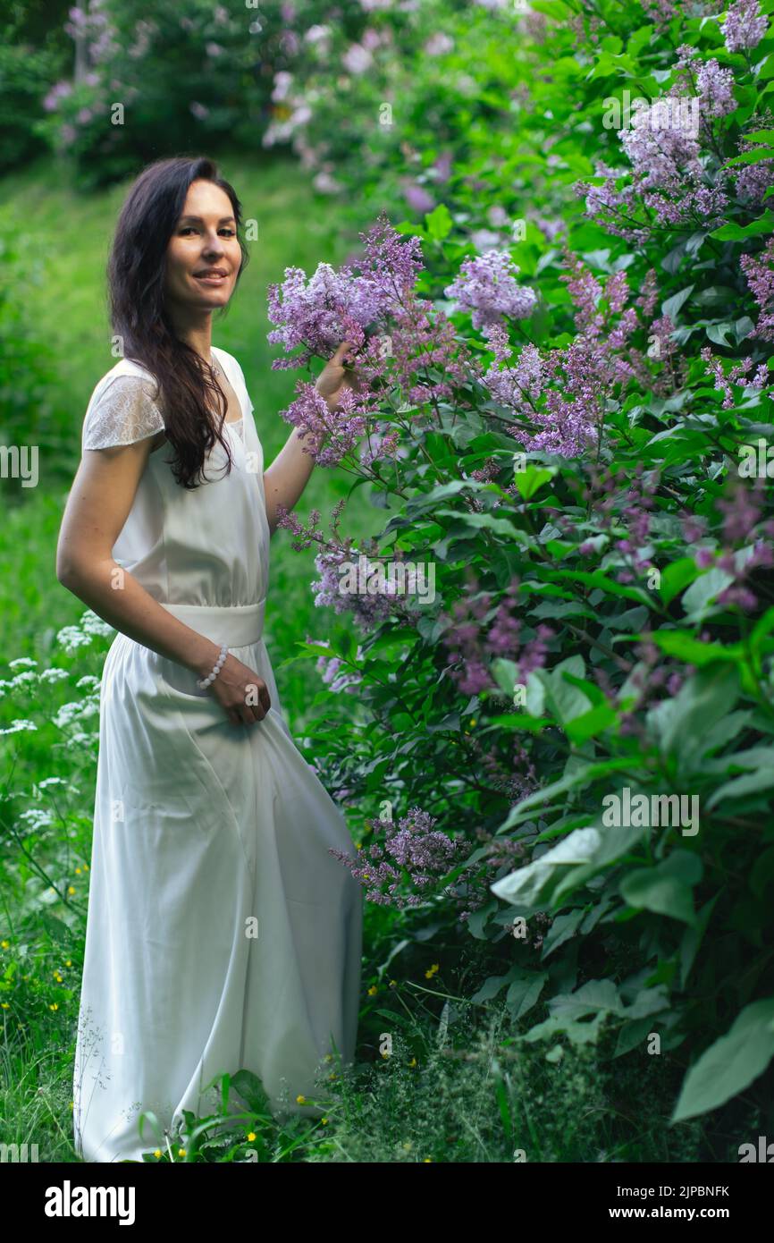 Porträt einer attraktiven Frau, umgeben von Fliederbüschen. Frühling und Sommer, saisonale Fotos. Vertikales Foto. Stockfoto