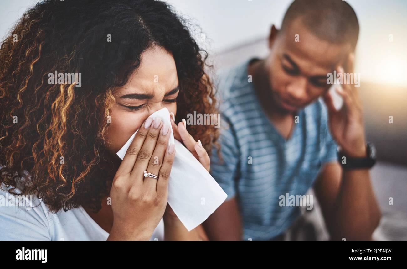 Die Grippesaison ist da. Eine junge Frau bläst ihre Nase mit ihrem Freund, der im Hintergrund geerregt aussieht. Stockfoto