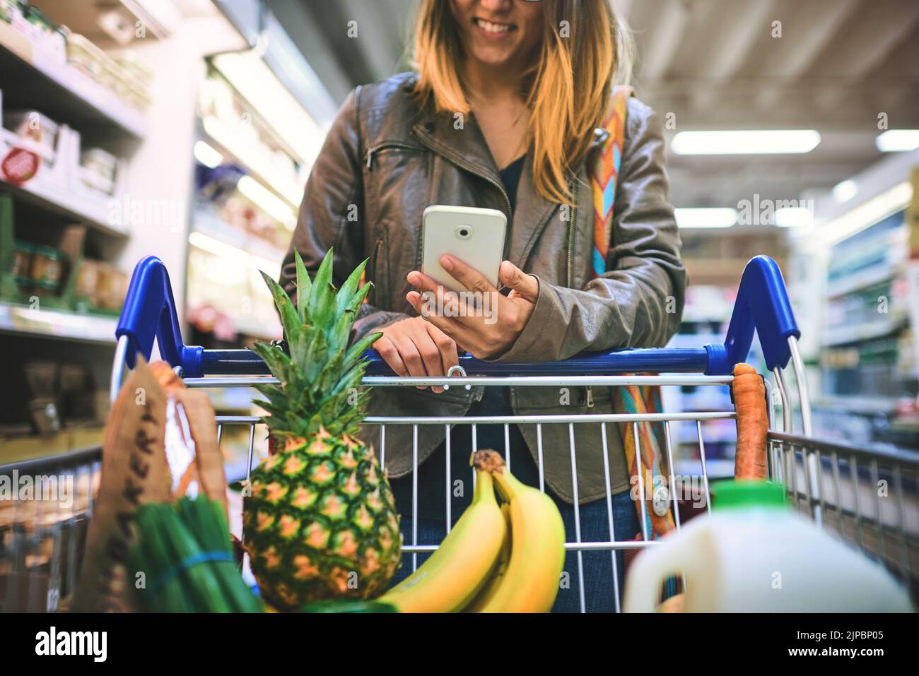 Ihre kleine Einkaufsassistentin. Eine Frau, die ein Mobiltelefon in einem Lebensmittelgeschäft benutzt. Stockfoto