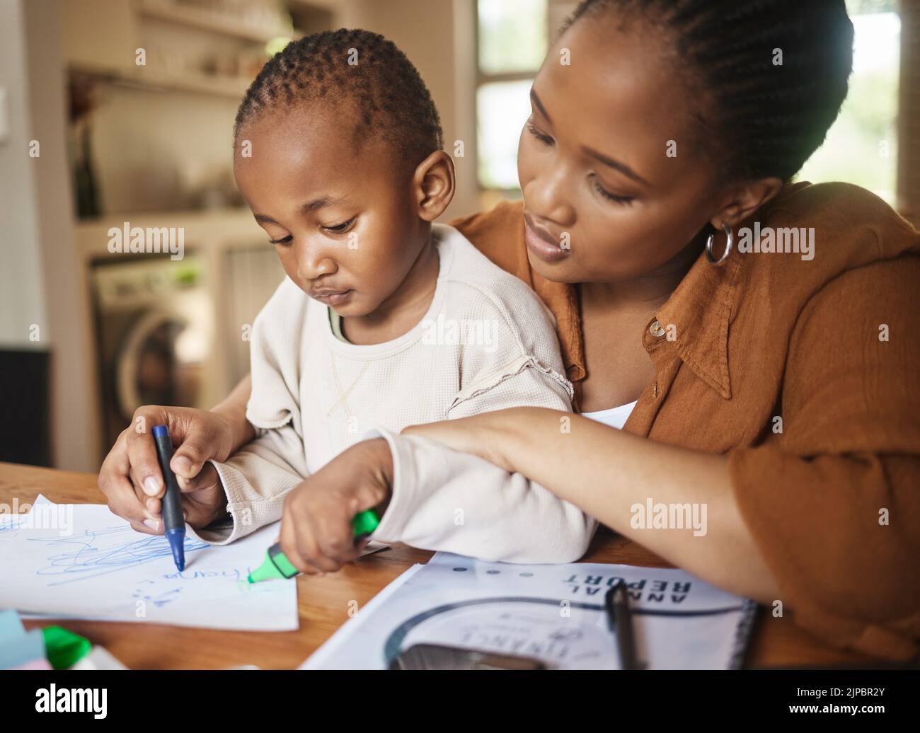 Afrikanische Mutter und kleines Kind zeichnen sich zu Hause am Schreibtisch zusammen. Fürsorgliche, arbeitende Frau, die der Familie Zeit lässt, mit dem Kind zu spielen. Lustig und lehrreich Stockfoto