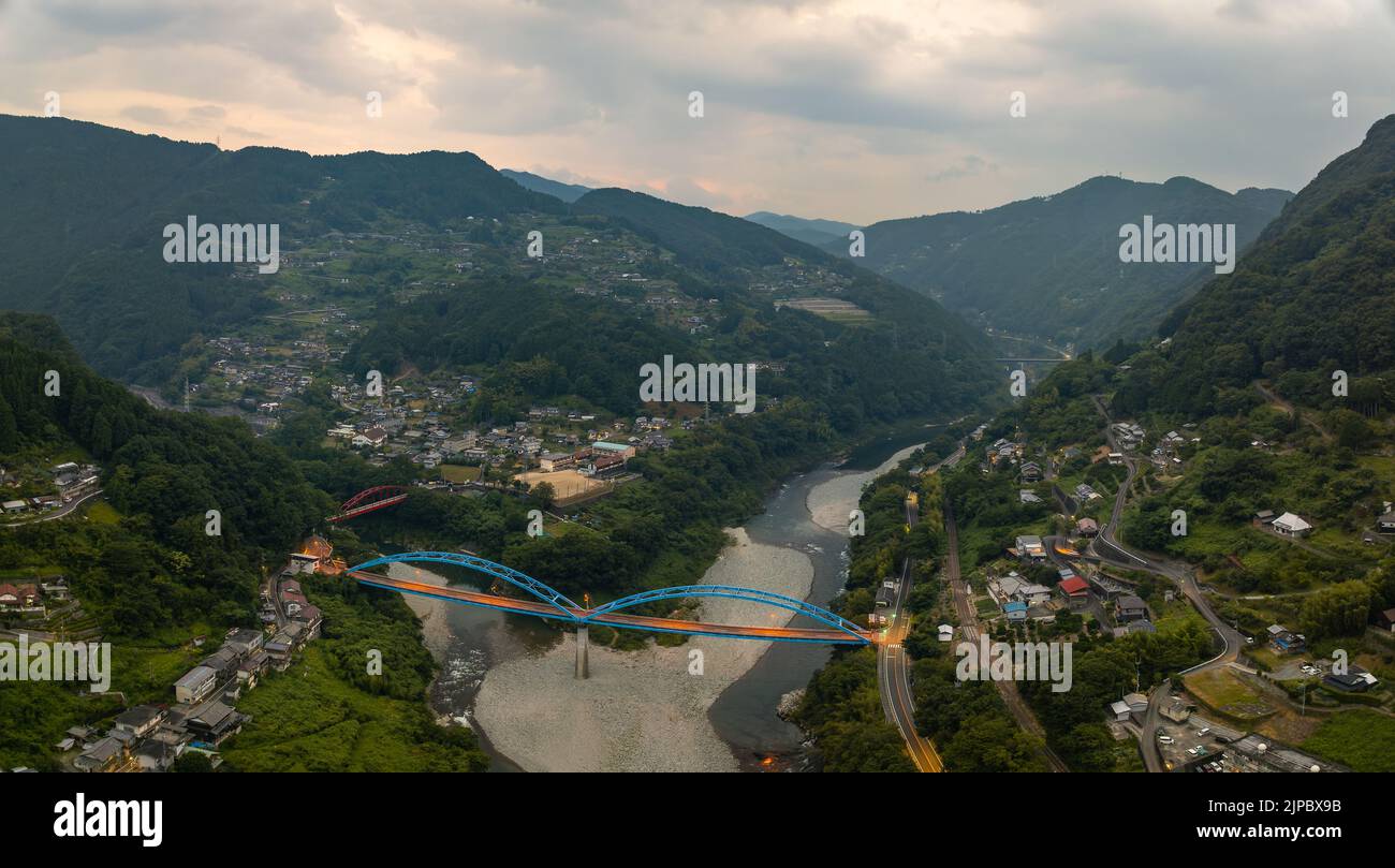 Panorama-Luftaufnahme der blauen Brücke, die ländliche Bergstädte in der Dämmerung verbindet Stockfoto