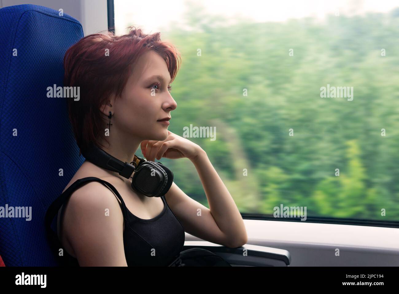 Mädchen fährt in einem Pendlerzug und blickt aus dem Fenster auf eine natürliche Landschaft, die in Bewegung verschwommen ist Stockfoto