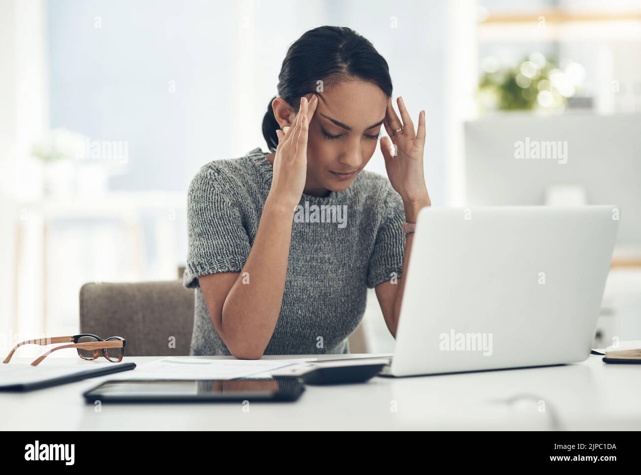 Kopfschmerzen, müde und gestresste junge Geschäftsfrau mit finanziellen Problemen auf dem Laptop am Schreibtisch sitzend. Professionelle weibliche Buchhalterin in der Buchhaltung Stockfoto
