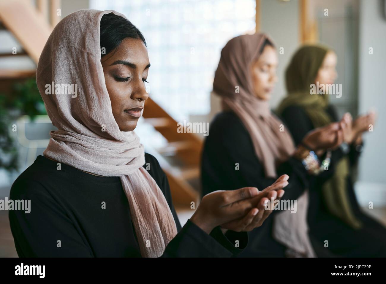 Betende, muslimische und junge Frauen üben in geschlossenen Räumen arabische, heilige und islamische Religion. Frauen tragen einen Hijab, während sie knien, um eine Ruhe zu üben Stockfoto