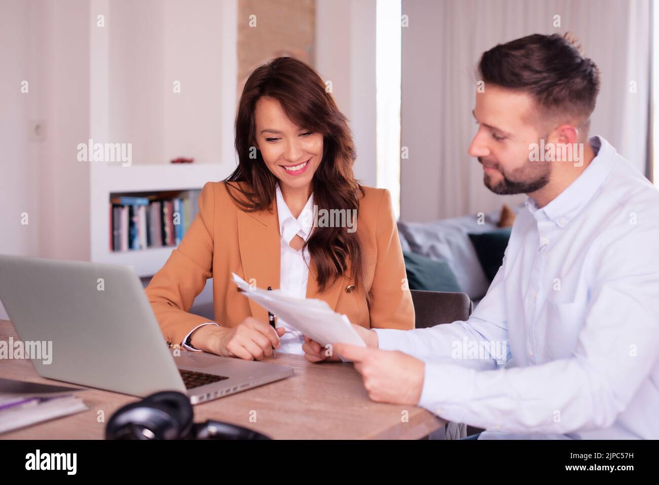 Geschäftsfrau und Geschäftsmann, die Dokumente betrachten, während sie hinter einem Laptop am Schreibtisch sitzen. Teamarbeit. Stockfoto