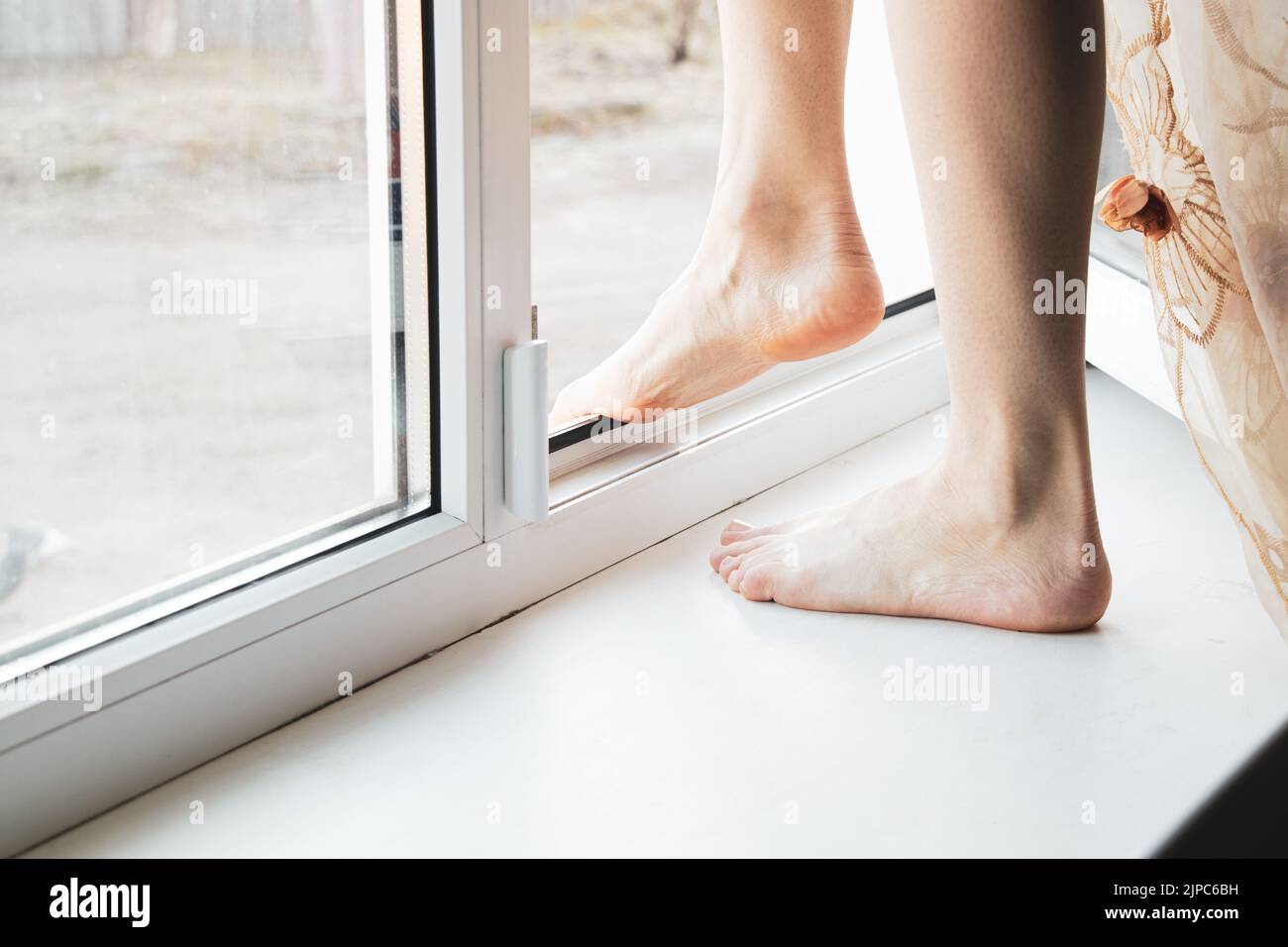 Ein junges Mädchen steht auf dem Fenster ihrer Wohnung, beging Selbstmord, sprang durch die Fenster, Depression und Selbstmord von Menschen, Füße im Wind Stockfoto