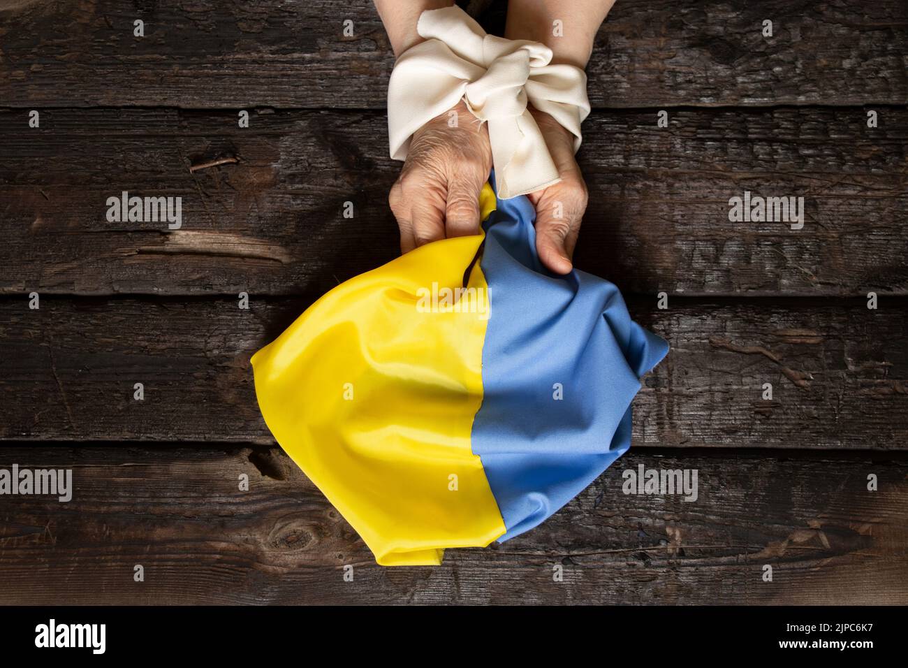 Hände einer ukrainischen Frau, mit einem weißen Seil gebunden, die eine gelbe und blaue Flagge der Ukraine auf einem hölzernen Hintergrund hält, Folter der Ukrainer an den Händen Stockfoto