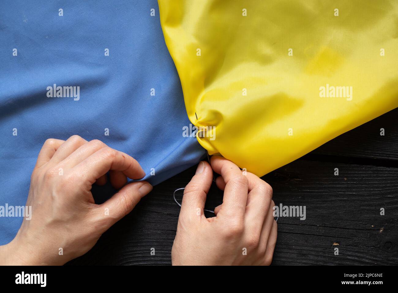 Weibliche Hände einer ukrainischen Frau nähen die Nationalflagge der Ukraine gelb-blau am Tisch zu Hause in der Ukraine, Patriot, stoppen den Krieg in der Ukraine Stockfoto