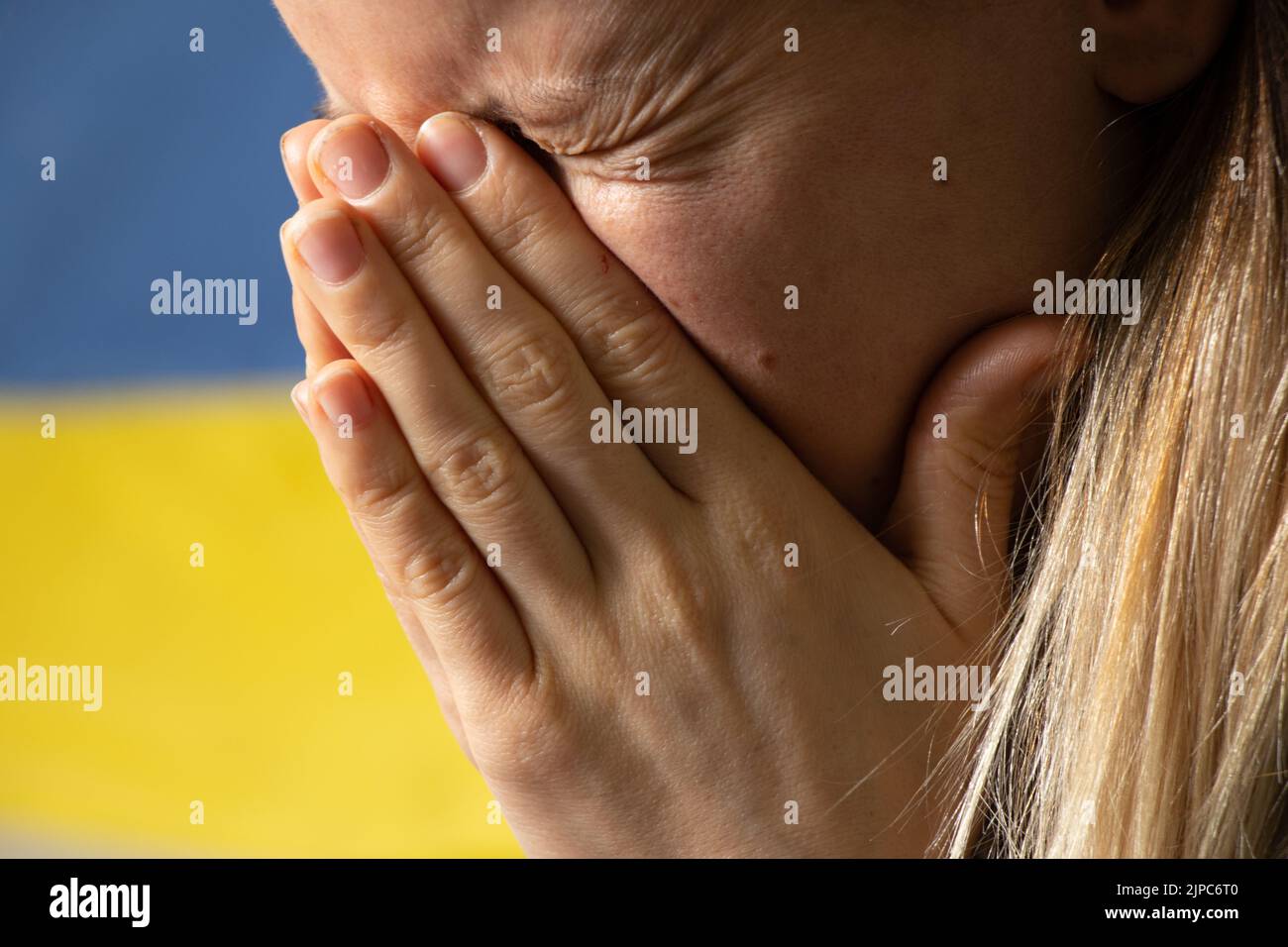 Ukrainische Frau weint vor Trauer und Angst vor dem Hintergrund der Flagge der Ukraine, Angst und Verzweiflung der Menschen in der Ukraine Stockfoto