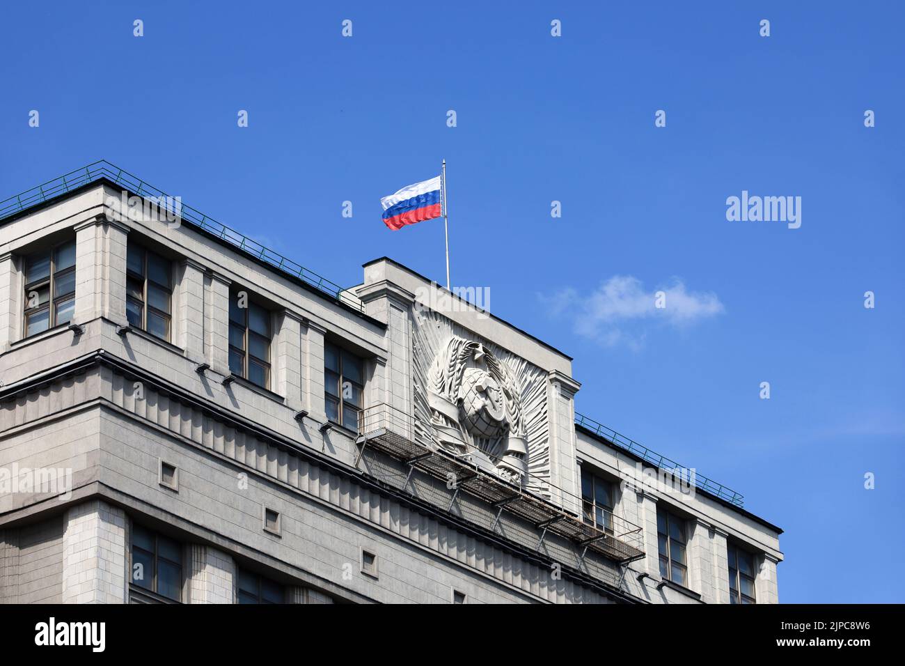 Parlamentsgebäude in Moskau mit russischer Flagge auf dem Hintergrund des blauen Himmels. Fassade der russischen Staatsduma mit sowjetischem Wappen, russische Autorität Stockfoto