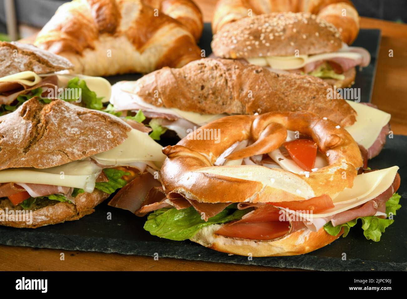 Im Restaurant werden verschiedene leckere Sandwiches mit Schinken, Käse und Gemüse auf Schiefertafeln auf einem Holztisch serviert Stockfoto