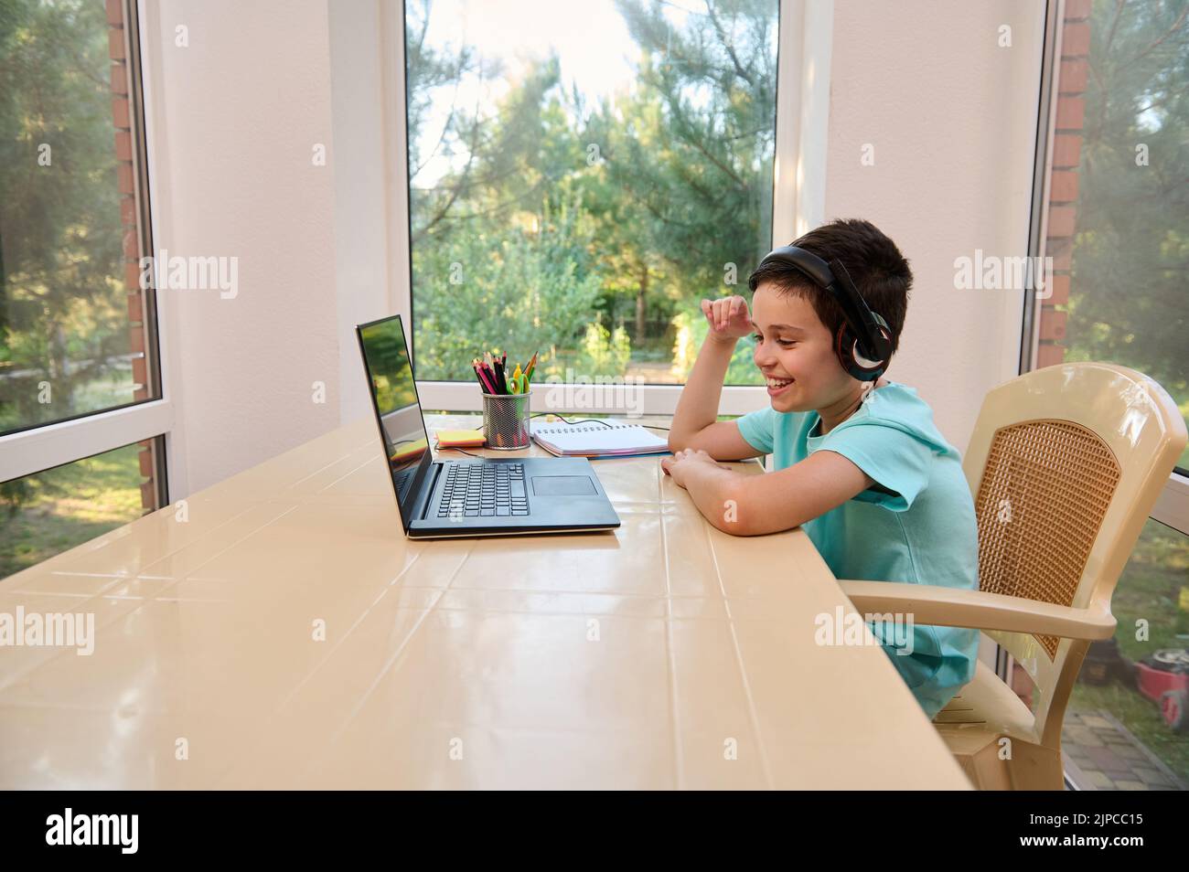 Ein gutaussehender, intelligenter Schuljunge, der von zu Hause aus lernt, sitzt am Laptop und kommuniziert per Videolink mit dem Lehrer. Stockfoto