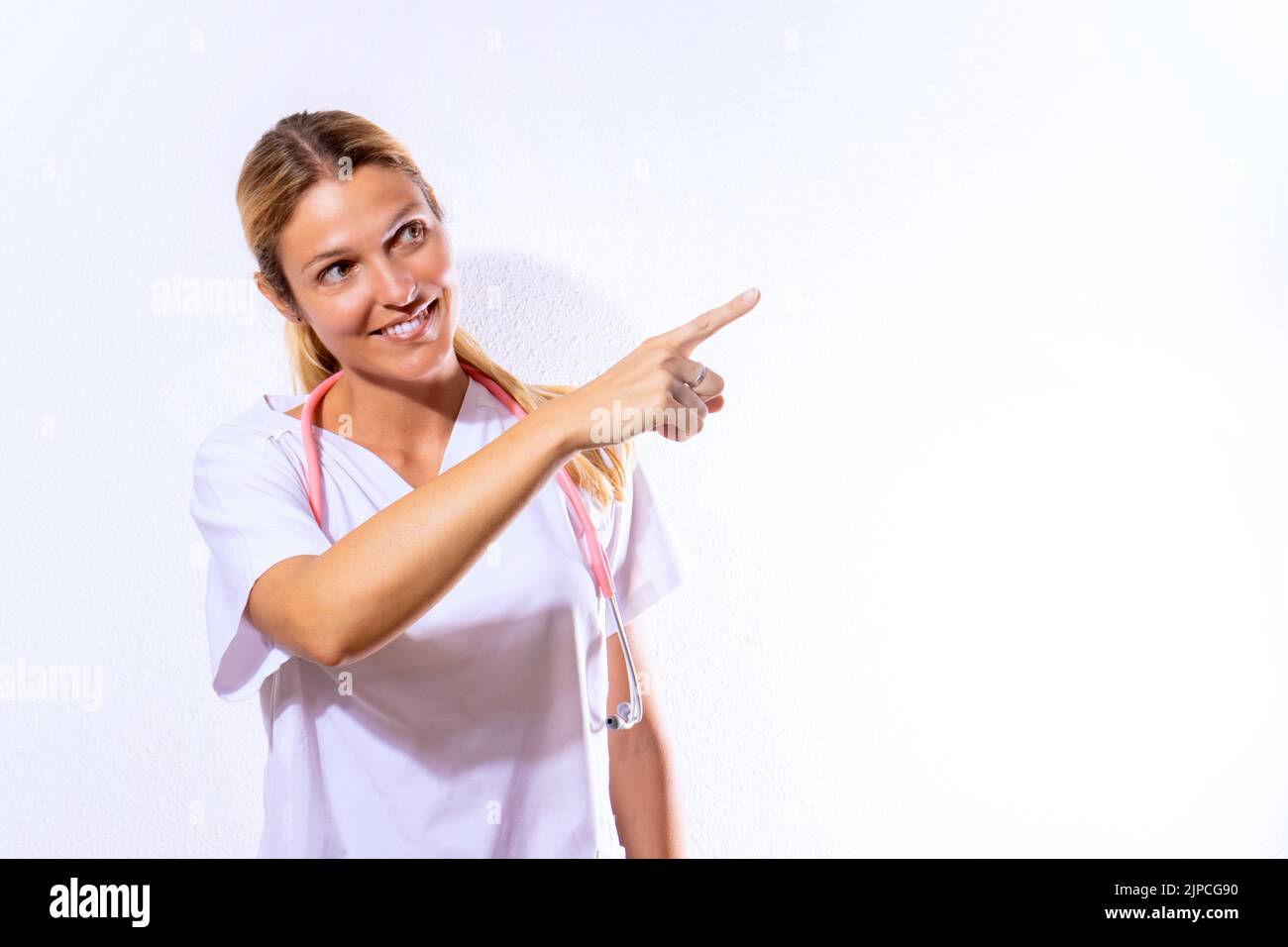 Krankenschwester in Krankenhauskittel und Stethoskop gekleidet zeigt. Sanitärkonzept. Weißer strukturierter Hintergrund und Kopierbereich Stockfoto