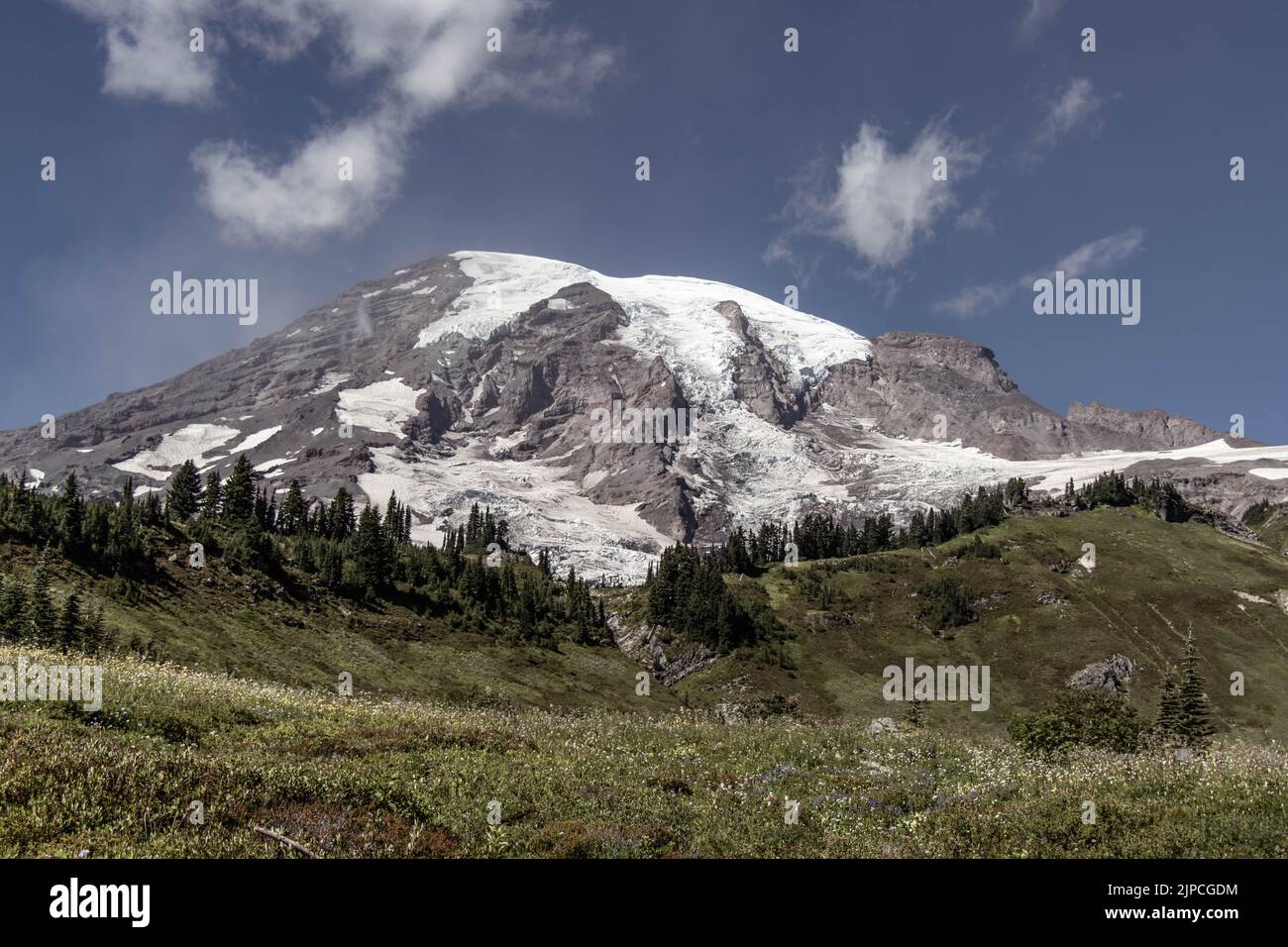 Die Landschaft der grünen Hügel und verschneiten Berggipfel unter dem blauen Himmel Stockfoto