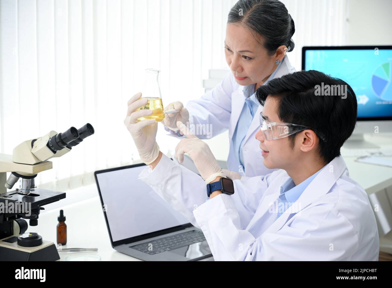 Professionelle asiatische leitende weibliche medizinische Vorgesetzte, die zusammen mit einem jungen männlichen Medizintechniker im Büro eine medizinische Flüssigkeit testet und arbeitet. Stockfoto
