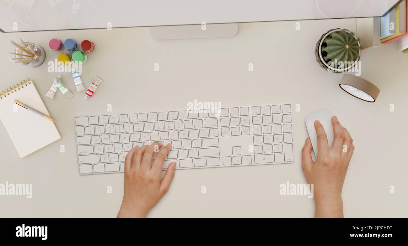 Moderner weißer Schreibtisch mit Bürozubehör und einer weiblichen Hand, die auf einer Computertastatur tippt. Draufsicht. Stockfoto