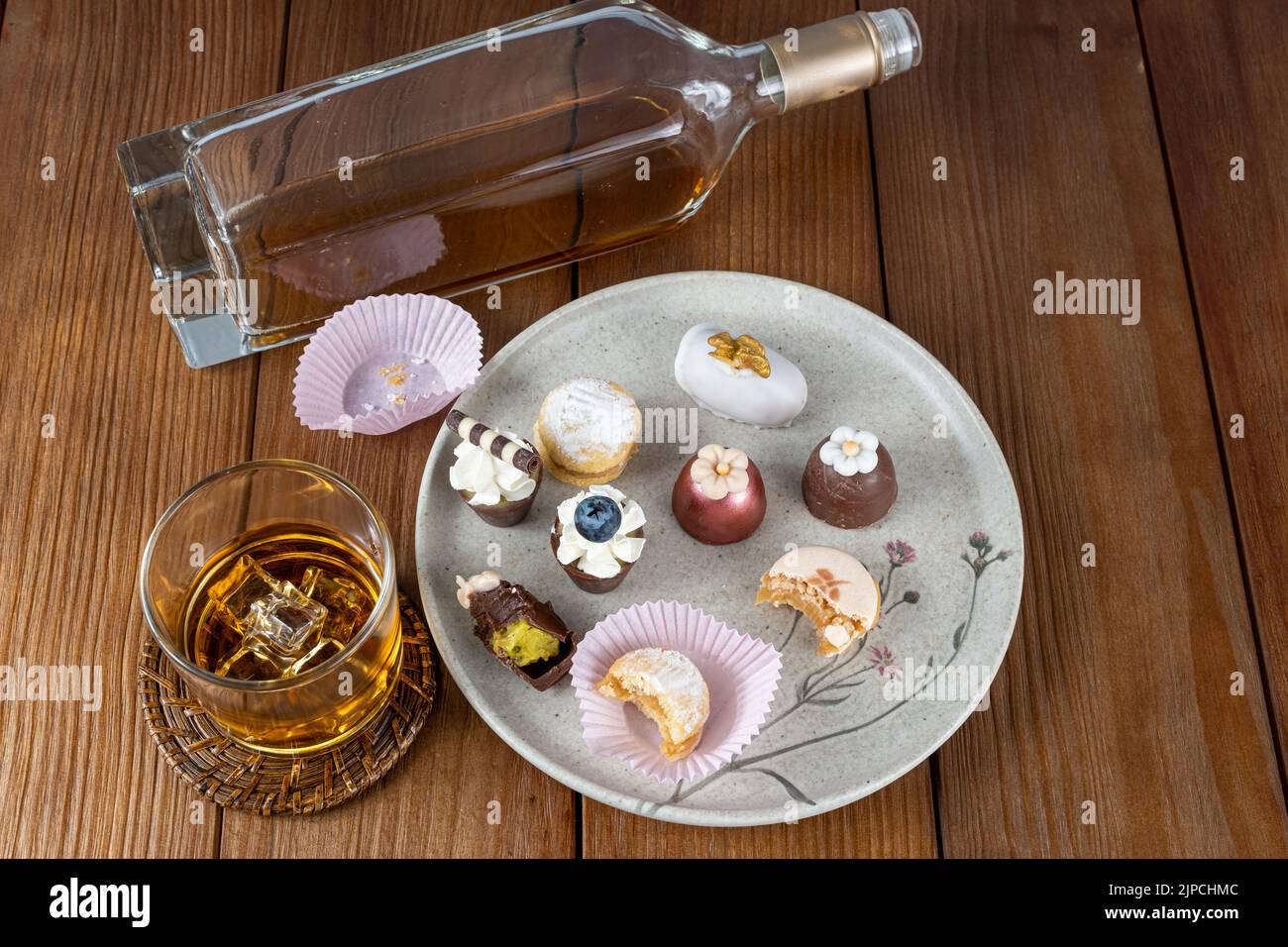 Kleines Schokoladenglas mit Schlagsahne und Heidelbeere, daneben Walnusskameo, Trüffel, Macaron- und Whiskey-Glas und Bottle top-Ansicht. Stockfoto