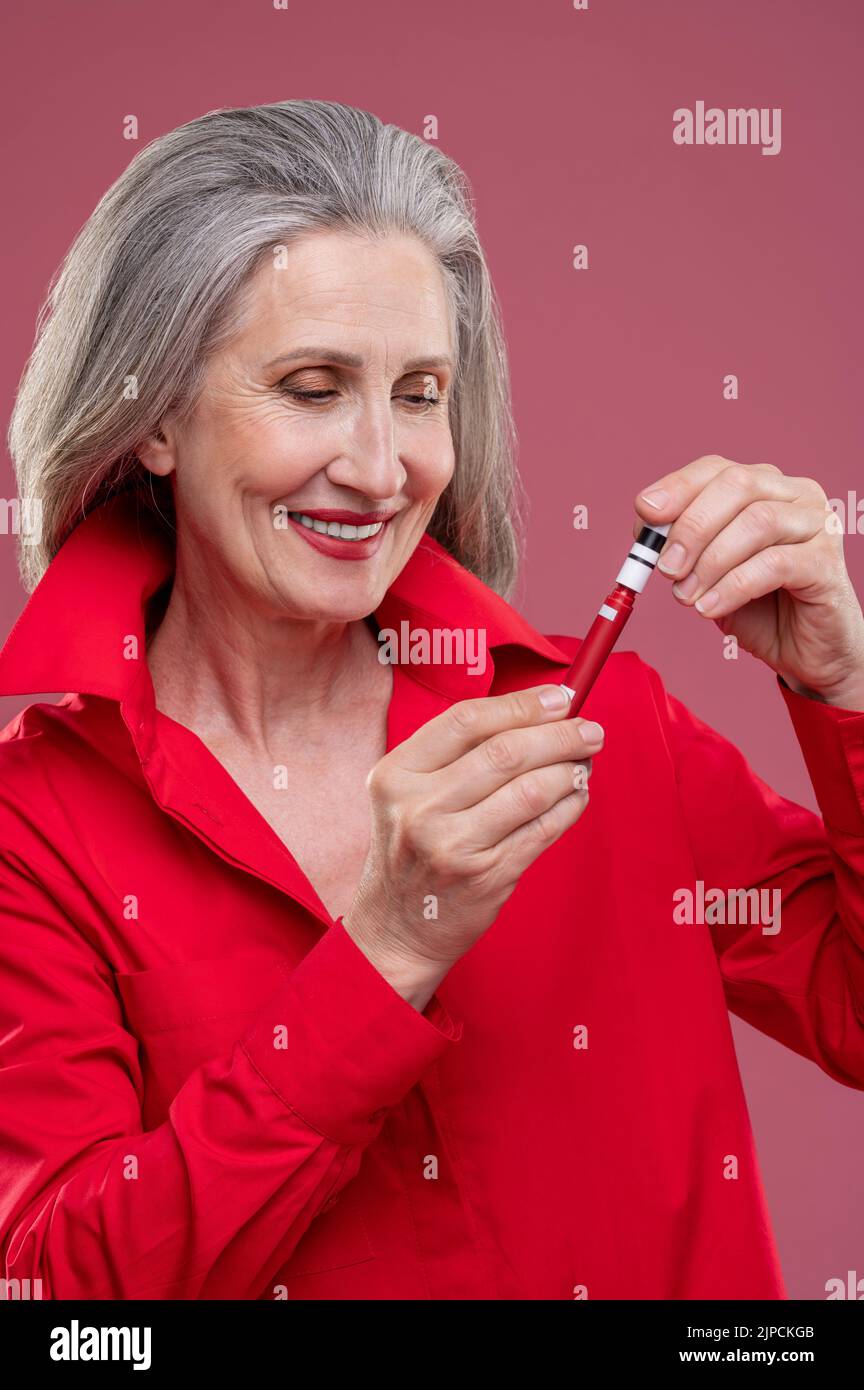 Gut aussehende reife Frau in Rot, die Glanz auf ihre Lops setzt Stockfoto