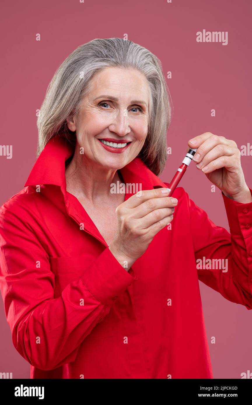 Gut aussehende reife Frau in Rot, die Glanz auf ihre Lops setzt Stockfoto