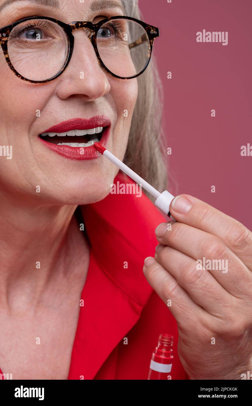 Gut aussehende Frau mittleren Alters, die Lippenglanz auf ihre Lippen setzt Stockfoto