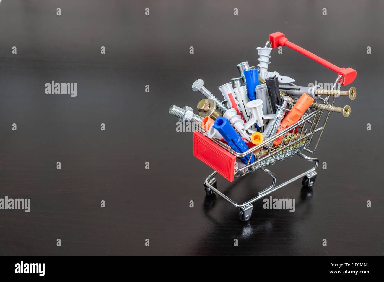 Verschiedene Arten von Befestigungselementen in einem Supermarktwagen. Platz für Text oder Logo. Konzept: Lagerung von Befestigungselementen. Dunkler Hintergrund. Stockfoto