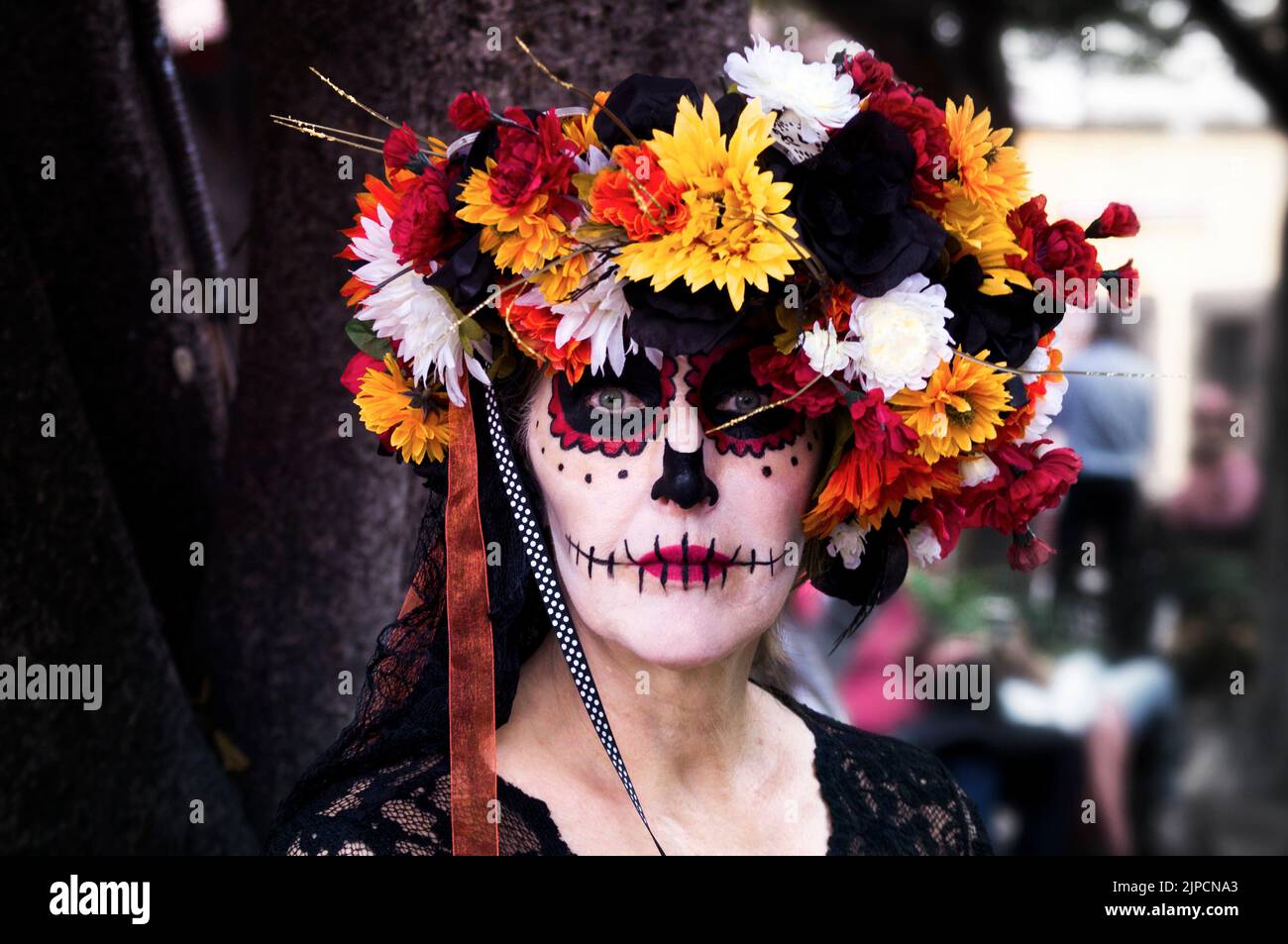 Ein wunderschönes Porträt einer Frau, die am Tag des Todes ein farbenfrohes Totenschädel-Make-up und eine Blumenkrone trägt Stockfoto