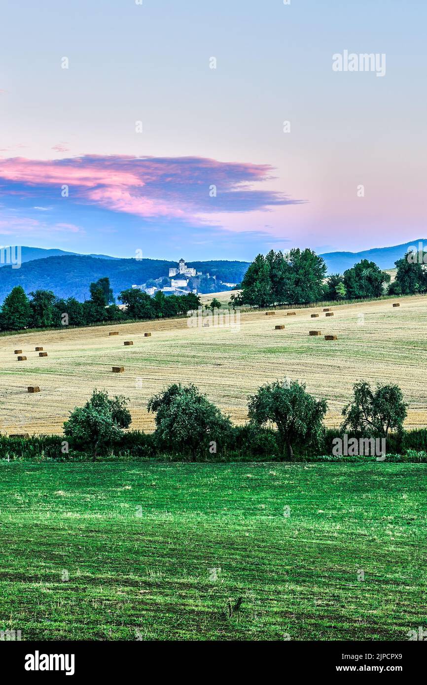 Slowakische ländliche Landschaft mit einer Burg im Hintergrund nach Sonnenuntergang. Mit Feld und Bäumen. Natürlicher Hintergrund, Tapete. Trencin, Orechove Slowakei Stockfoto