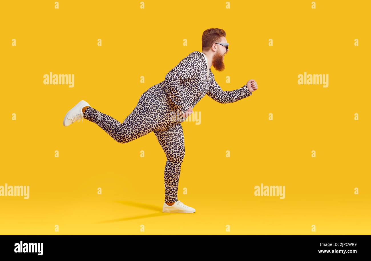 Witziger, exzentrischer, fetter Mann in Kleidung mit Leopardenmuster, der auf gelbem Hintergrund herumtollt. Stockfoto