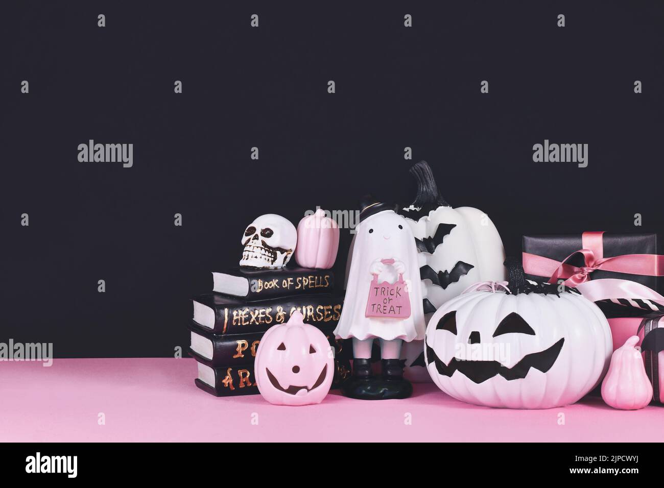 Pink-weißes Halloween Dekor mit schwarzen und weißen Kürbissen, Zauberbüchern und Spinnen auf schwarzem Hintergrund mit Kopierfläche Stockfoto