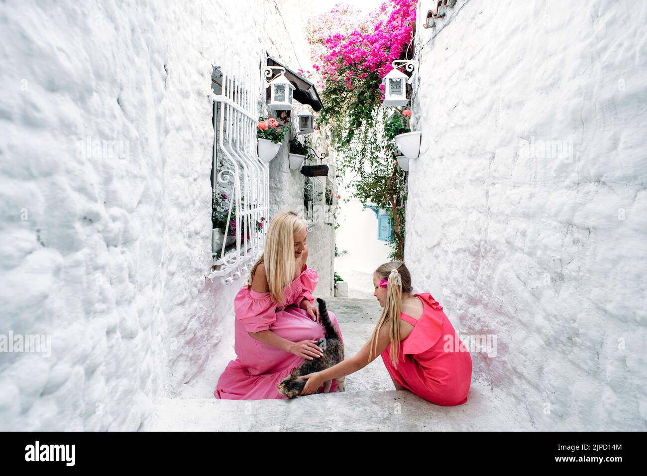 Mutter im mittleren Alter und Tochter eines blonden Teenagers, die auf der mittelalterlichen Straße von Marmaris, Türkei, mit einer nichthäuslichen Katze spielt. Ein Elternteil Stockfoto