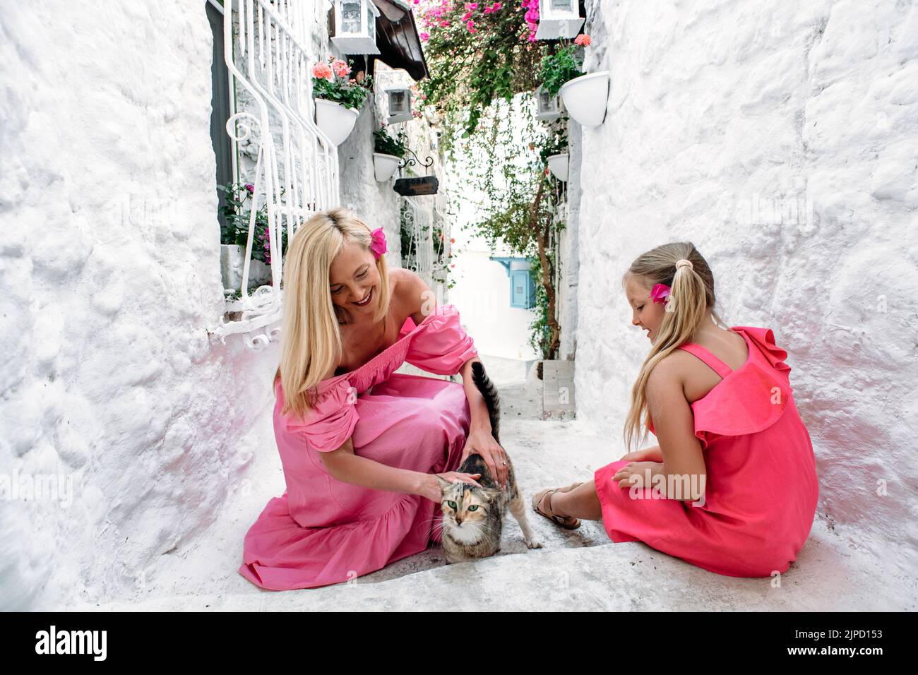 Mutter im mittleren Alter und Tochter eines blonden Teenagers, die auf der mittelalterlichen Straße von Marmaris, Türkei, mit einer nichthäuslichen Katze spielt. Ein Elternteil Stockfoto