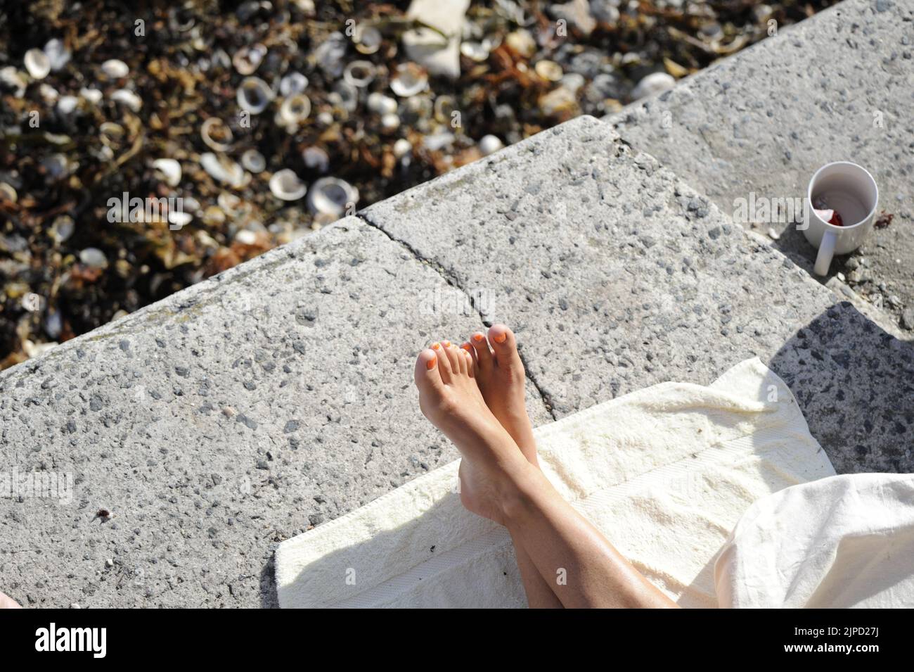 Füße Frau mit gekreuzten Beinen entspannen auf Hafenfront bei Sonnenschein auf Handtuch Stockfoto