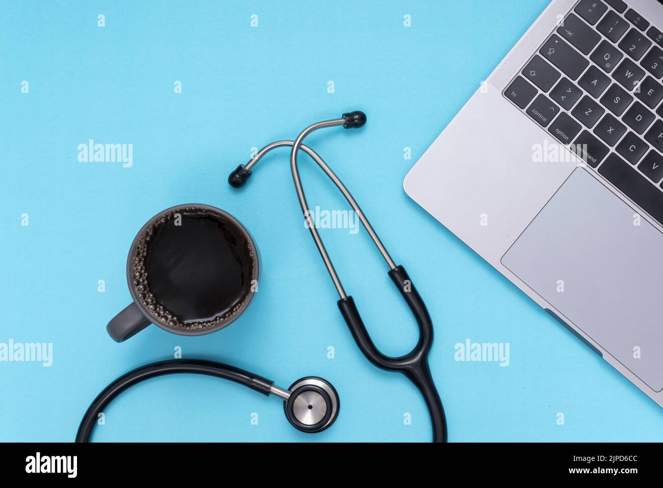 Schwarzes Stethoskop, Laptop, Kaffee, blauer isolierter Hintergrund Stockfoto
