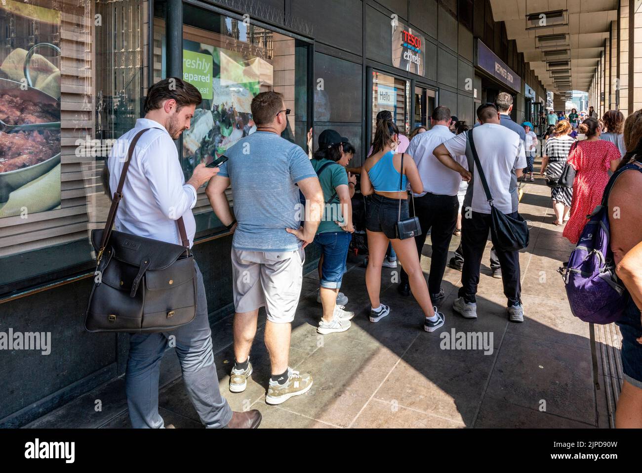 Menschen stehen vor dem Tesco Express Supermarkt in Westminster an dem heißesten Tag, der je in London, London, Großbritannien, aufgezeichnet wurde. Stockfoto