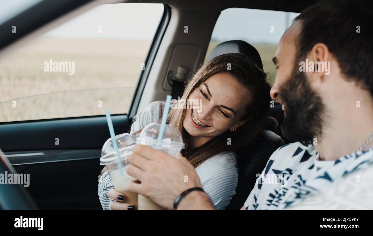 Kaukasische fröhliche Frau sitzt im Auto und trinkt Kaffee mit ihrem Freund, glückliches Paar mittleren Alters auf Reise Stockfoto