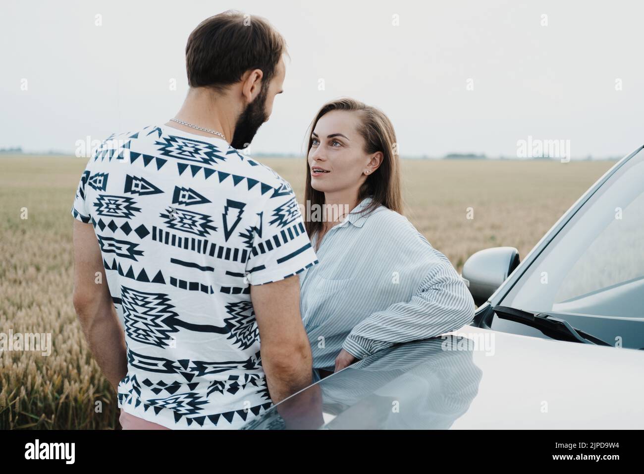Kaukasische Frau und Mann, die sich im Freien in der Nähe des Autos auf dem Feld unterhalten, Paar mittleren Alters auf einer Autofahrt Stockfoto