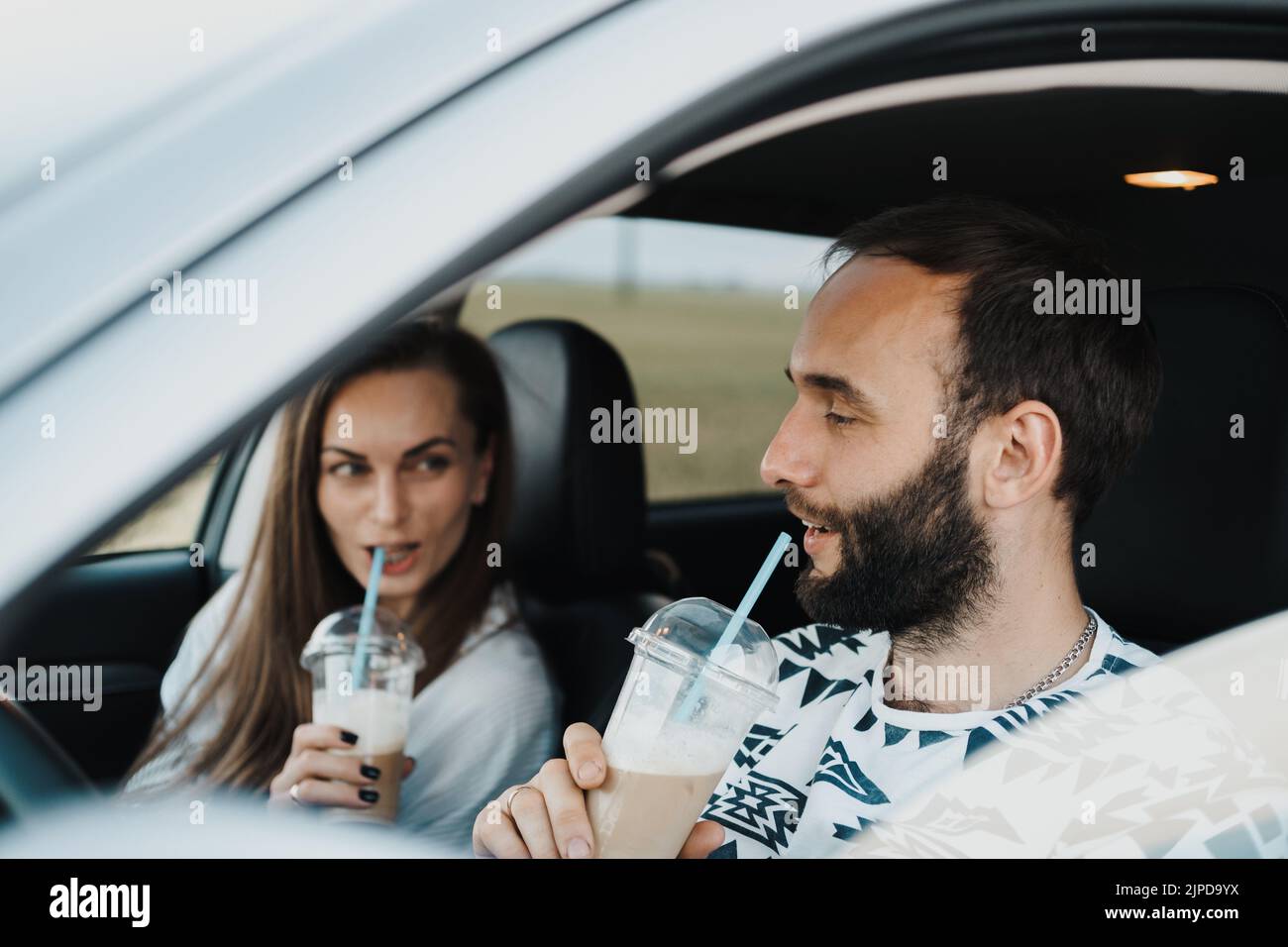 Kaukasischer gutaussehender Mann, der im Auto sitzt und Kaffee trinkt, mit Freundin, glückliches Paar mittleren Alters auf Autotour Stockfoto