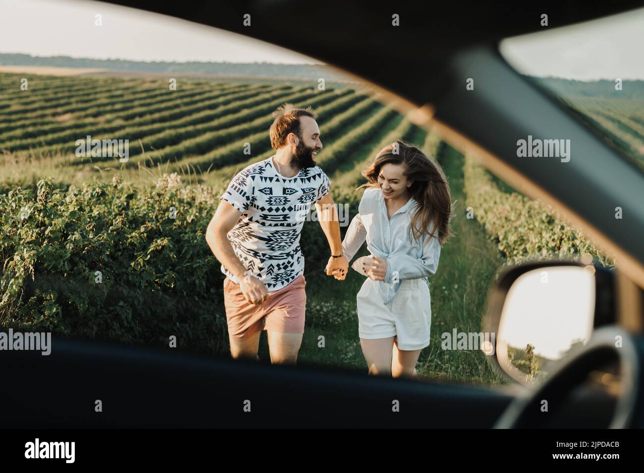 Blick durch das Autofenster, glückliches Paar mittleren Alters, das auf den wunderschönen Feldern läuft, kaukasischer Mann und Frau, die ihren Urlaub im Freien genießen Stockfoto