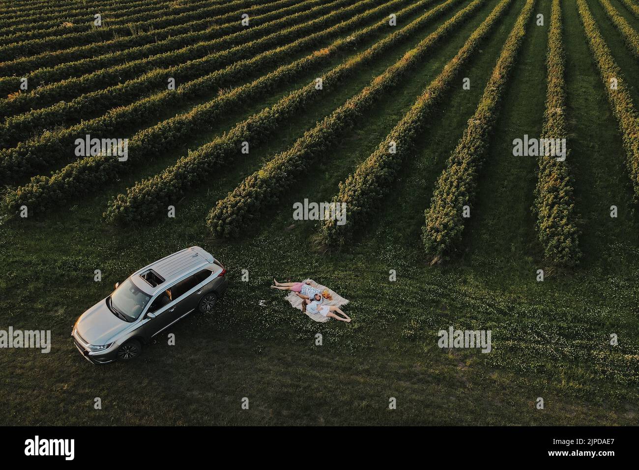 Luftaufnahme Paar genießen Picknick auf der Straße Reise in den schönen Feldern, Mann und Frau liegen auf einer Decke in der Nähe des SUV-Auto bei Sonnenuntergang Stockfoto